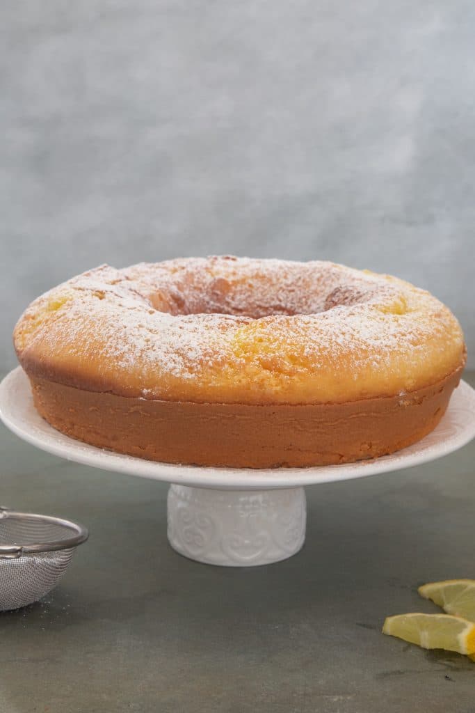 Lemon cake dusted with powdered sugar on a white cake stand.