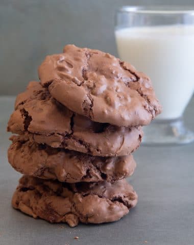 4 brownie drop cookies stacked with a glass of milk.