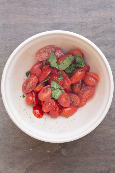 The tomatoes mixed with basil, oregano and oil in a bowl.