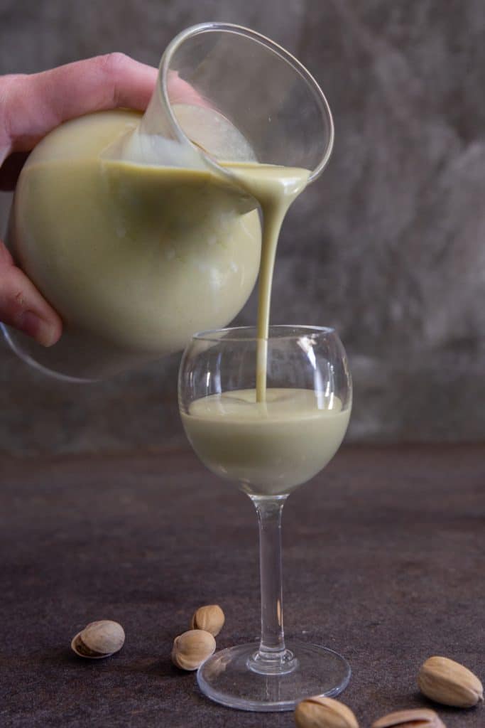 pouring pistachio liqueur in a glass.