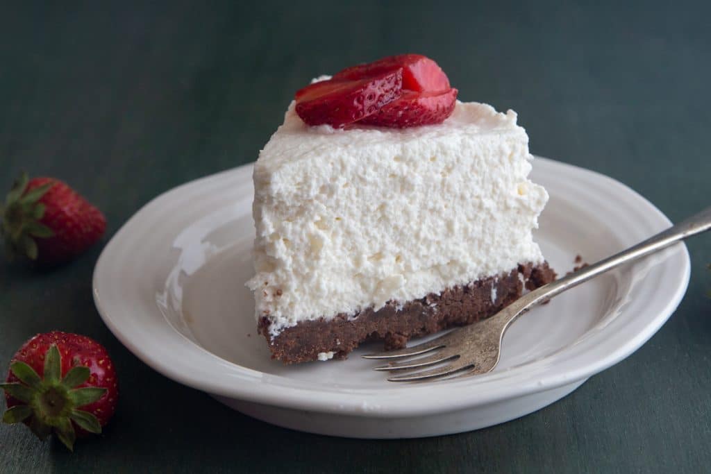A slice of cheesecake on a white plate with a silver fork.