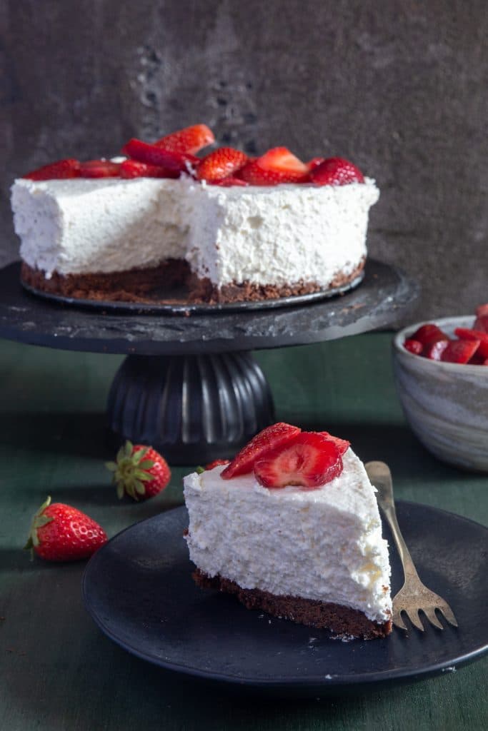 Ricotta cheesecake on a cake stand with a slice on a black plate.
