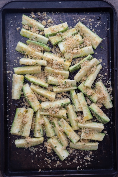 Unbaked zucchini on a black cookie sheet.