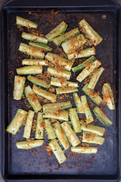 Baked zucchini on a black cookie sheet.