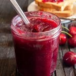 Cherry jam in a glass jar with a spoon.