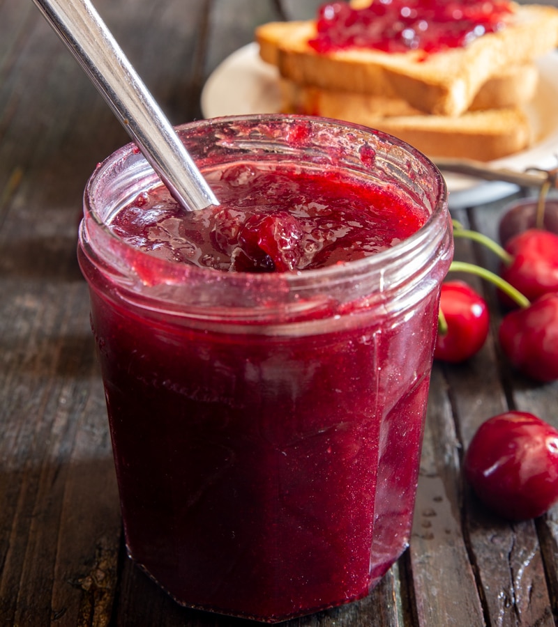 Cherry jam in a glass jar with a spoon.