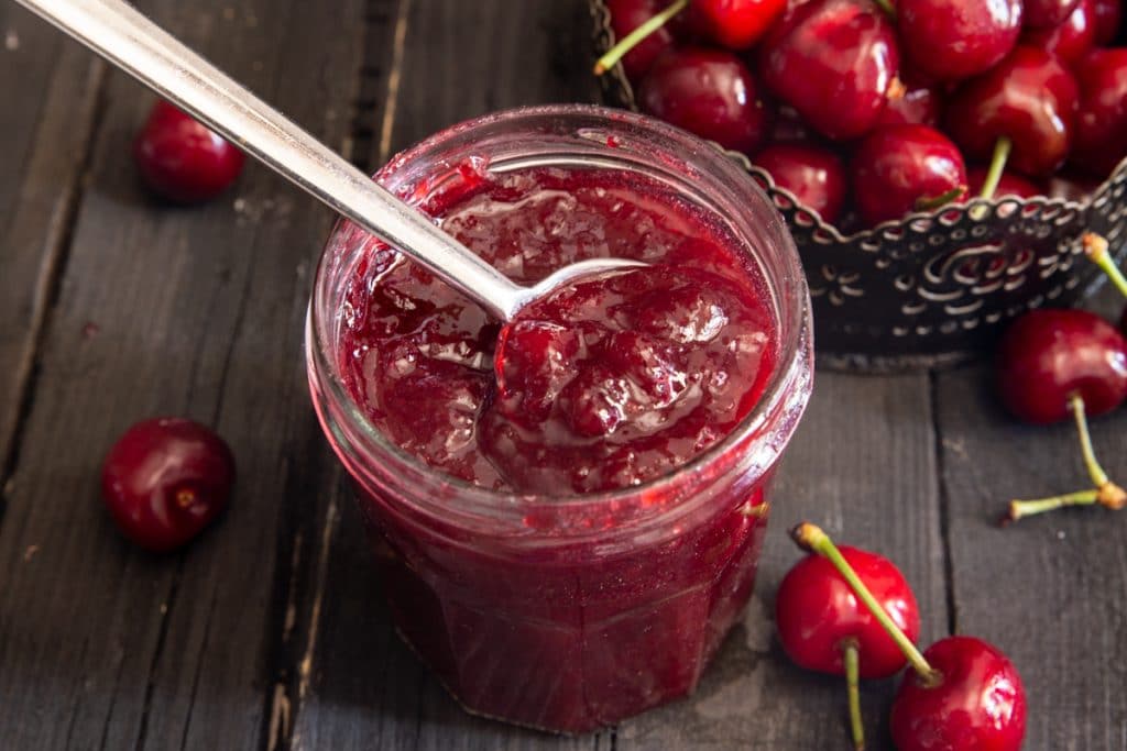 Cherry jam in a glass jar with a silver spoon.