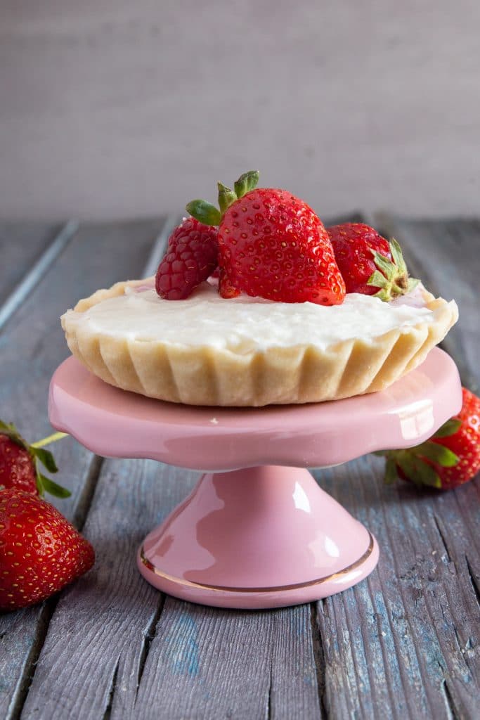 A cheesecake tart on a pink cake stand.