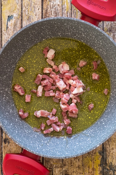 The pancetta and oil in a red pan.