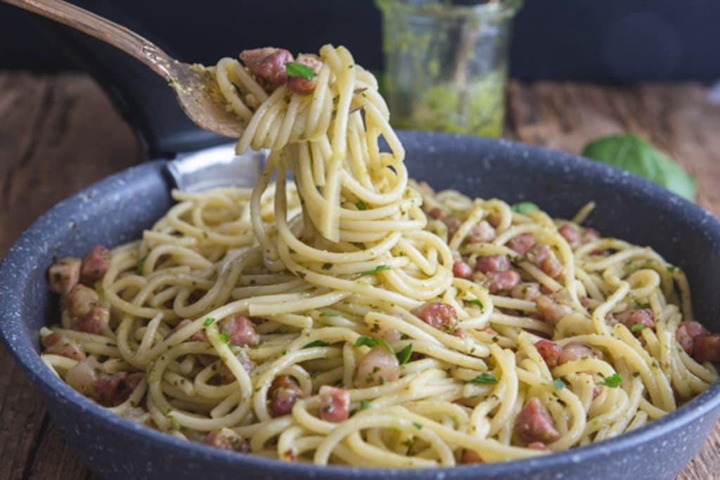 Pesto pasta in a black pan and some on a fork.