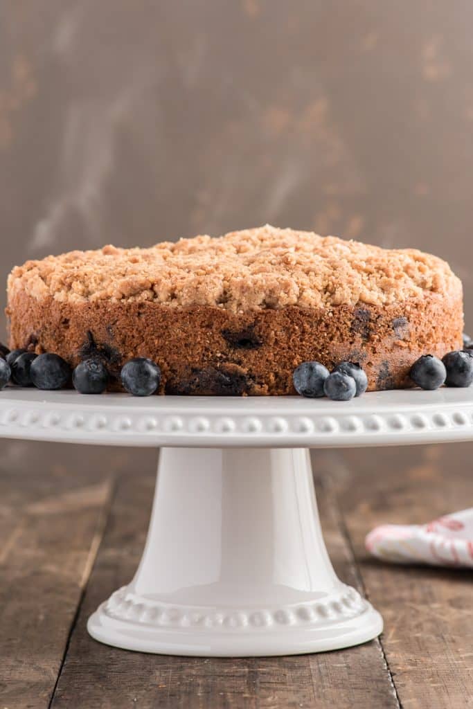 Blueberry crumb cake on a white stand.