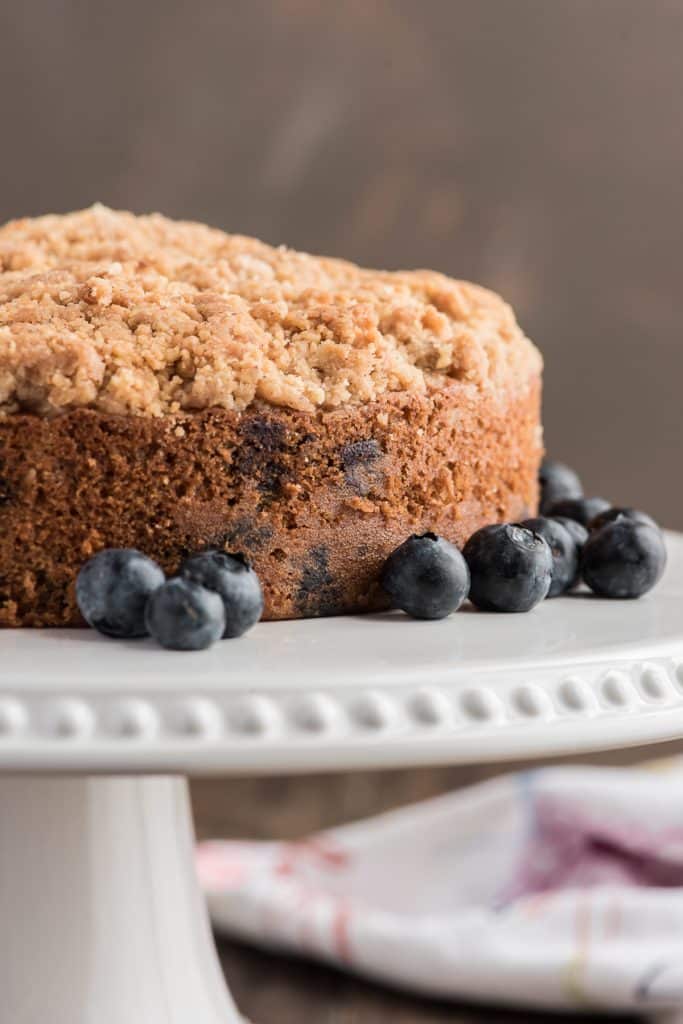 Blueberry crumb cake on a white cake stand.