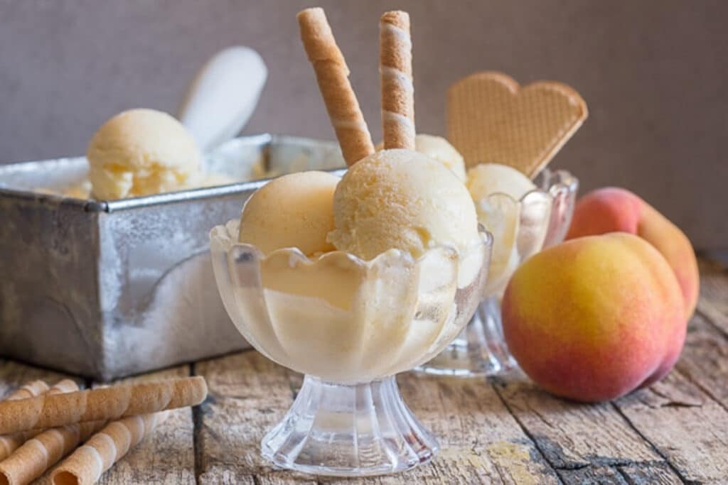 Peach ice cream in a bowl with fresh peaches.