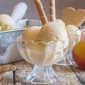 Peach ice cream in a bowl with fresh peaches.