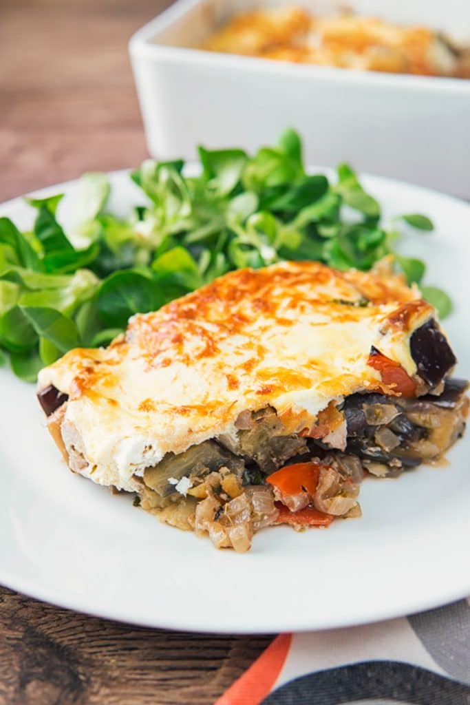 A slice of casserole on a white plate with salad.
