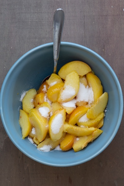 Peach slices mixed with sugar in a blue bowl.