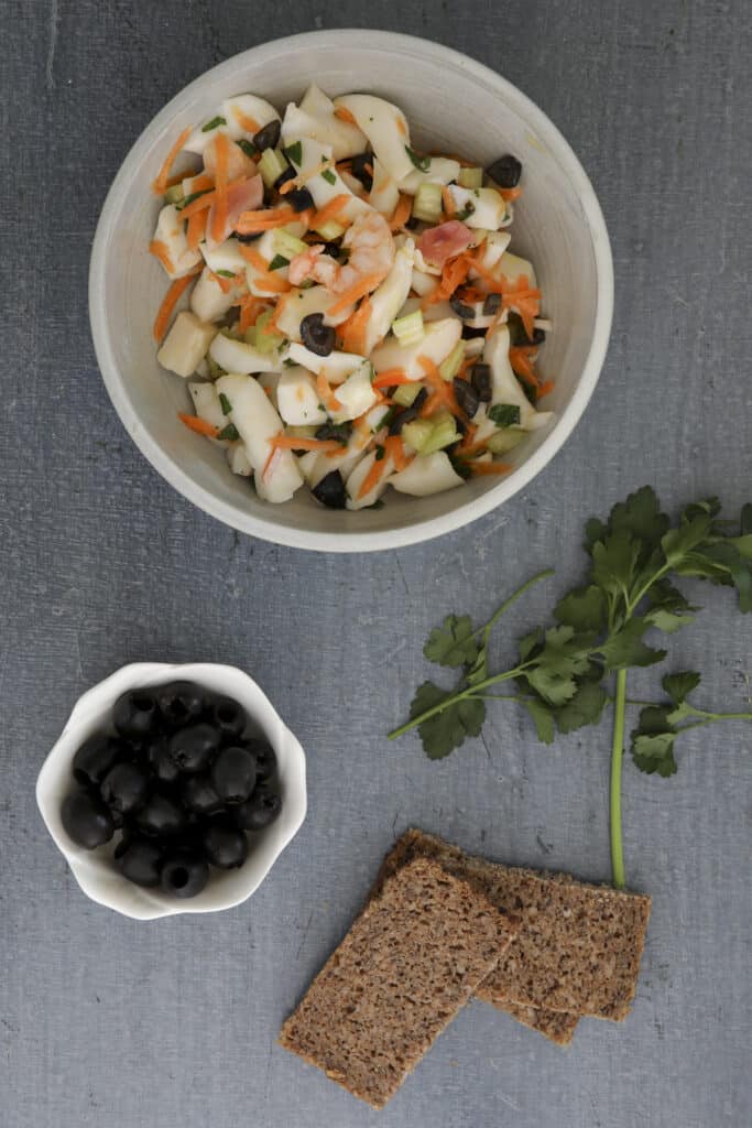 Seafood salad in a white bowl with olives in a small white bowl and three slices of bread.