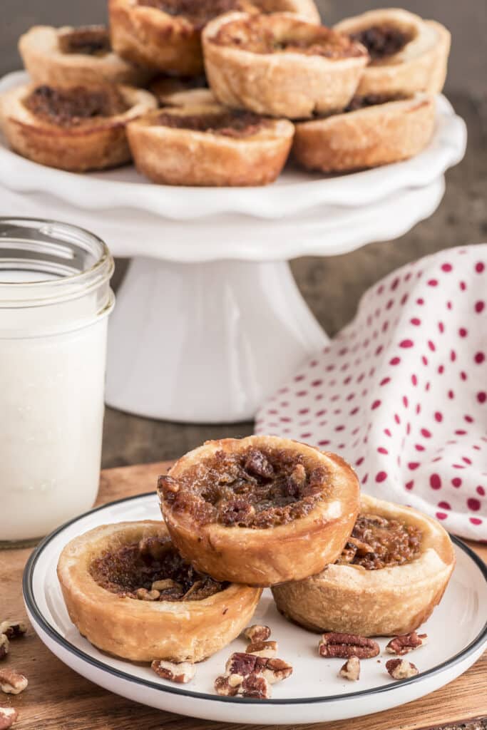 Butter tarts on a white cake stand and three on a white plate.
