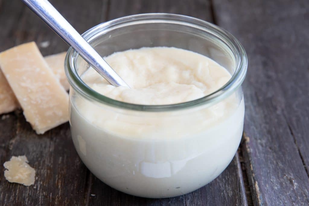 Parmesan cheese sauce and a spoon in a jar.