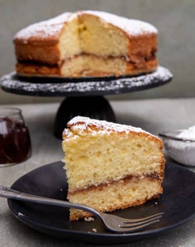 Jam cake with a slice cut on a black plate.