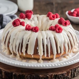 Cake with frosting and raspberries on a white cake plate.