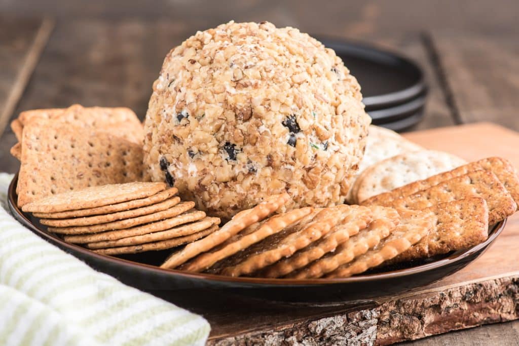 Cheese ball on a black plate with crackers.