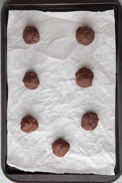 Cookie dough balls on parchment baking sheet.