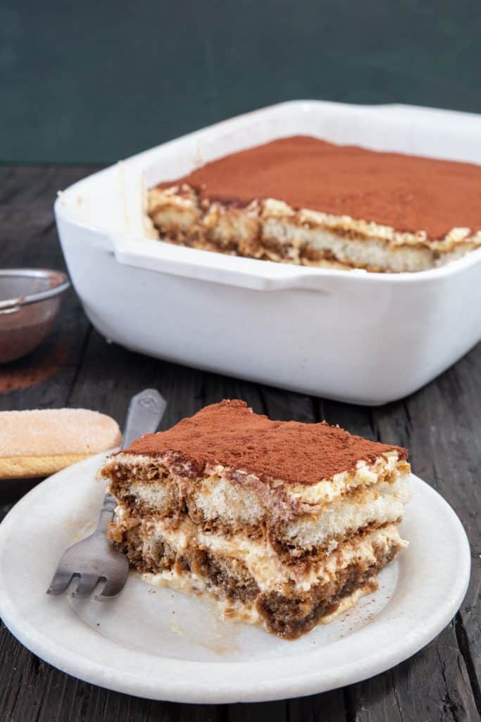 Tiramisu in a baking dish and a slice on a plate.