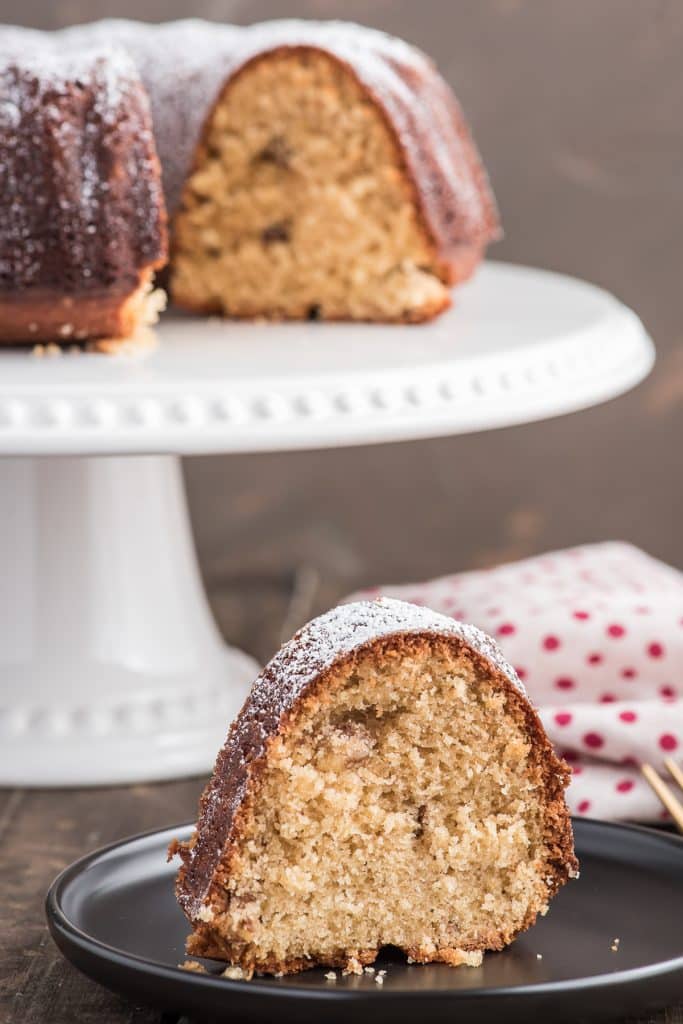 Brown sugar bundt cake on a white cake stand with a slice on a black plate.