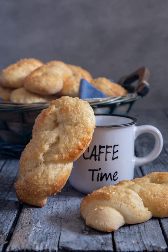 Cookies in a basket, one leaning on an espresso cup and one on the board.