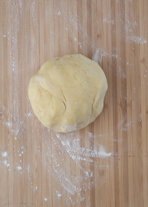 The dough formed in to a ball on a wooden board.
