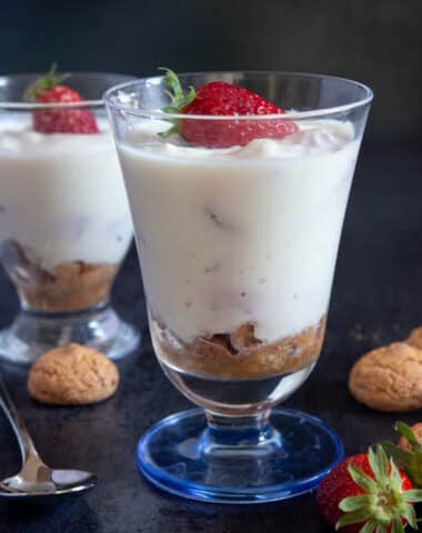 Two glasses of ricotta cream with a spoon, cookies and strawberries.