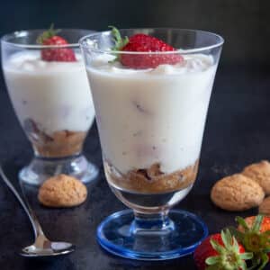 Two glasses of ricotta cream with a spoon, cookies and strawberries.