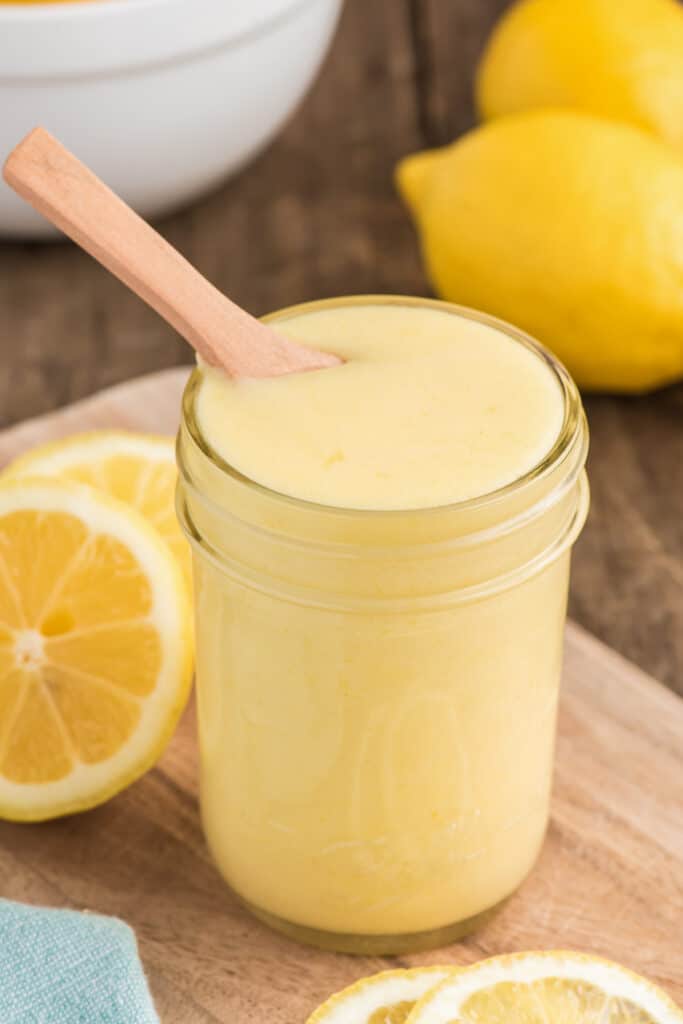 Lemon curd in a jar with a wooden spoon.