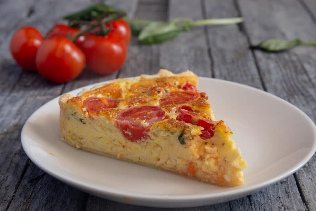 A slice of quiche on a white plate.