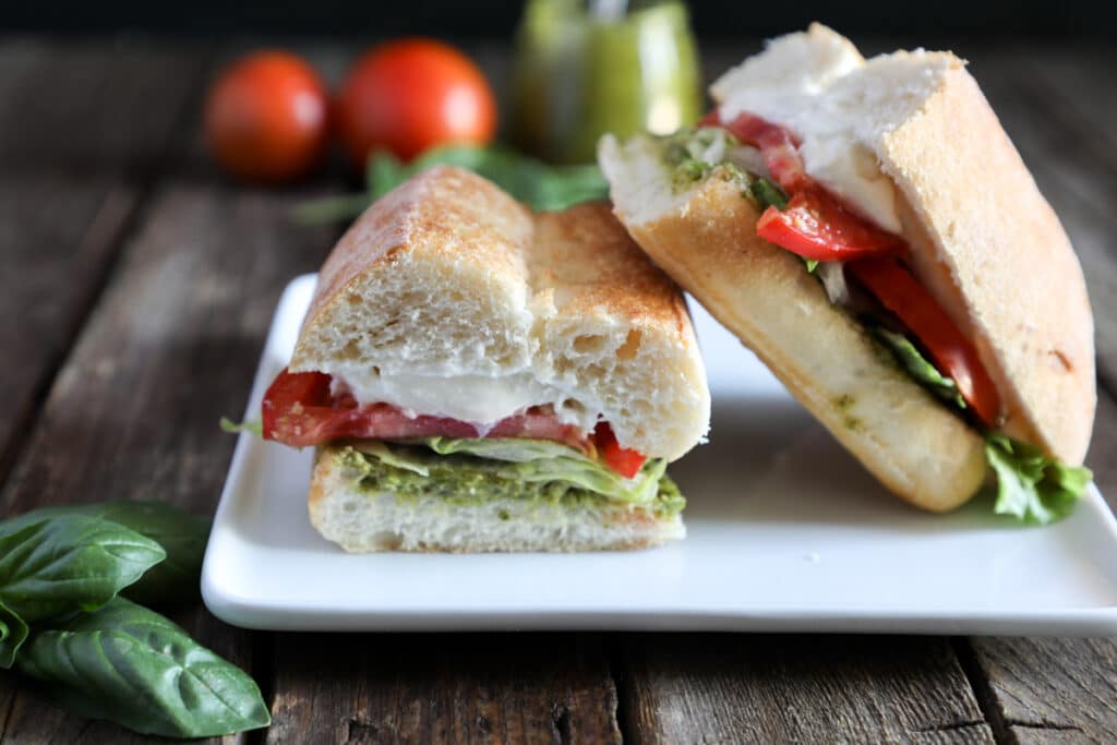 Panino on a white plate with pesto and tomatoes in the back ground.