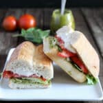 Panino on a white plate with pesto and tomatoes in the back ground.