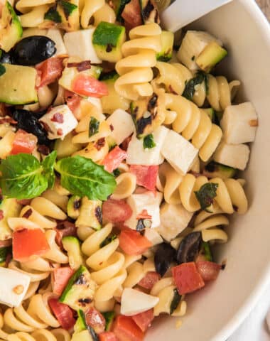 Pasta salad up close in a white bowl with a spoon.