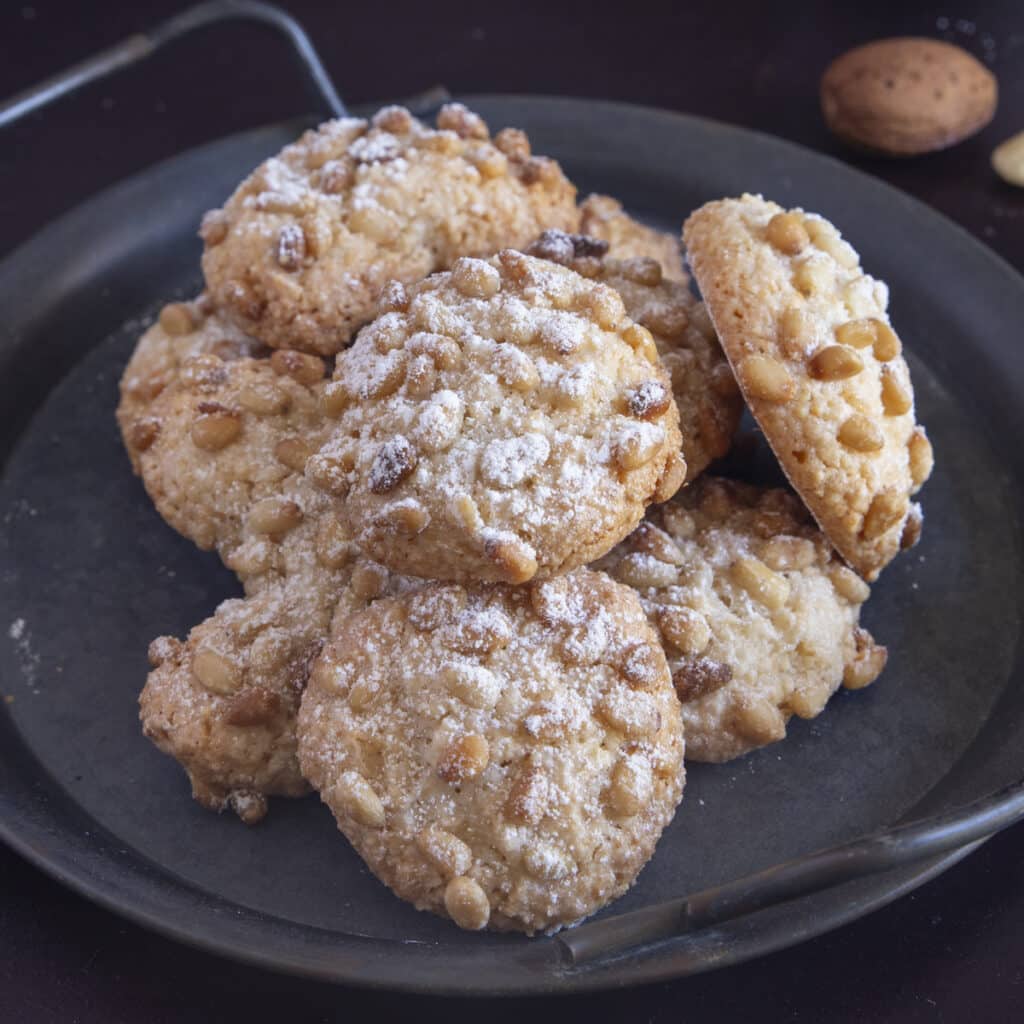 Pignoli cookies on a black plate.