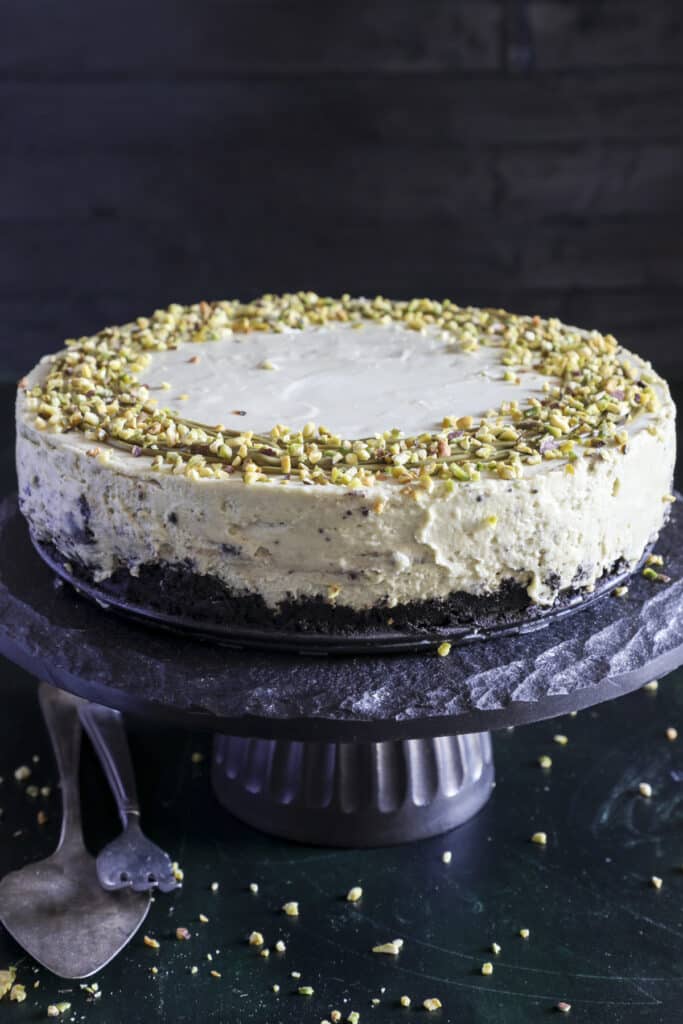 Pistachio cheesecake on a black cake stand.