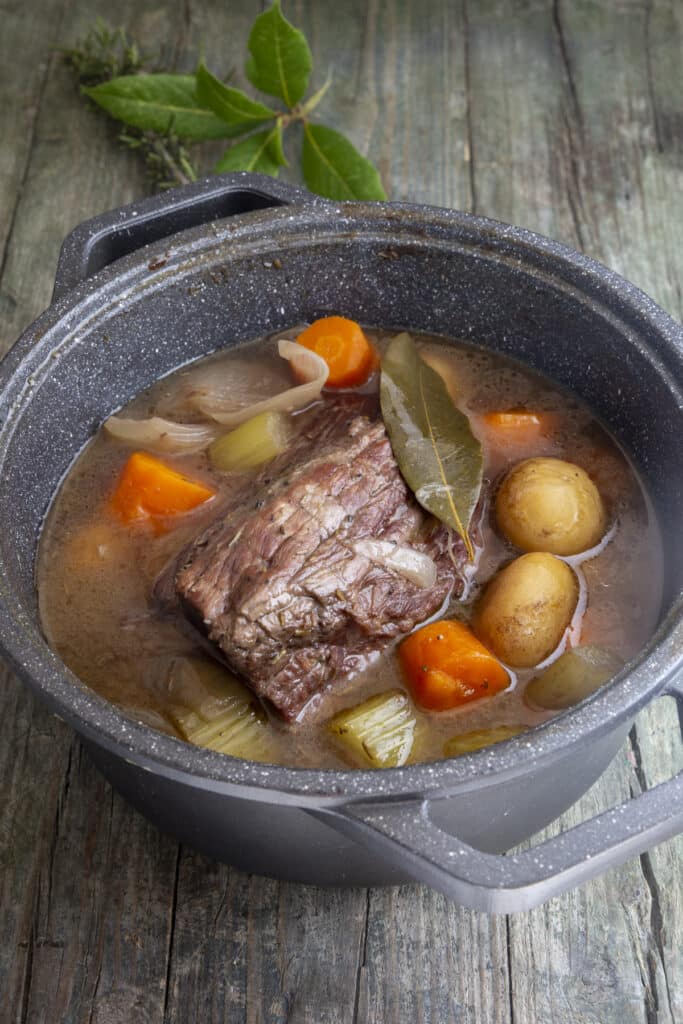 Pot roast with vegetables in a black pot.