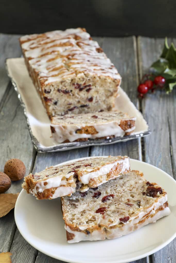 Cranberry bread on a white plate with two slices on a white plate.