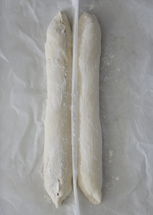 The bread shaped into baguettes on the parchment paper.