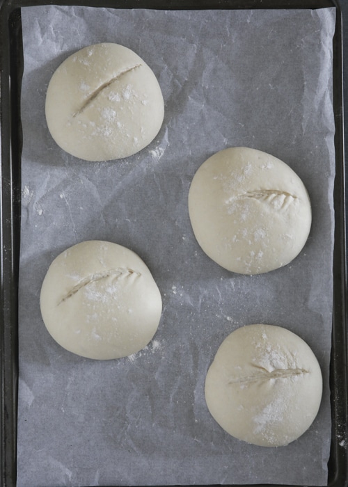 The dough balls risen on the parchment paper baking sheet.
