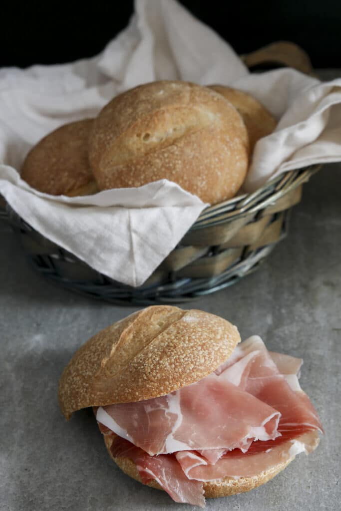 Buns in a basket and one with prosciutto.