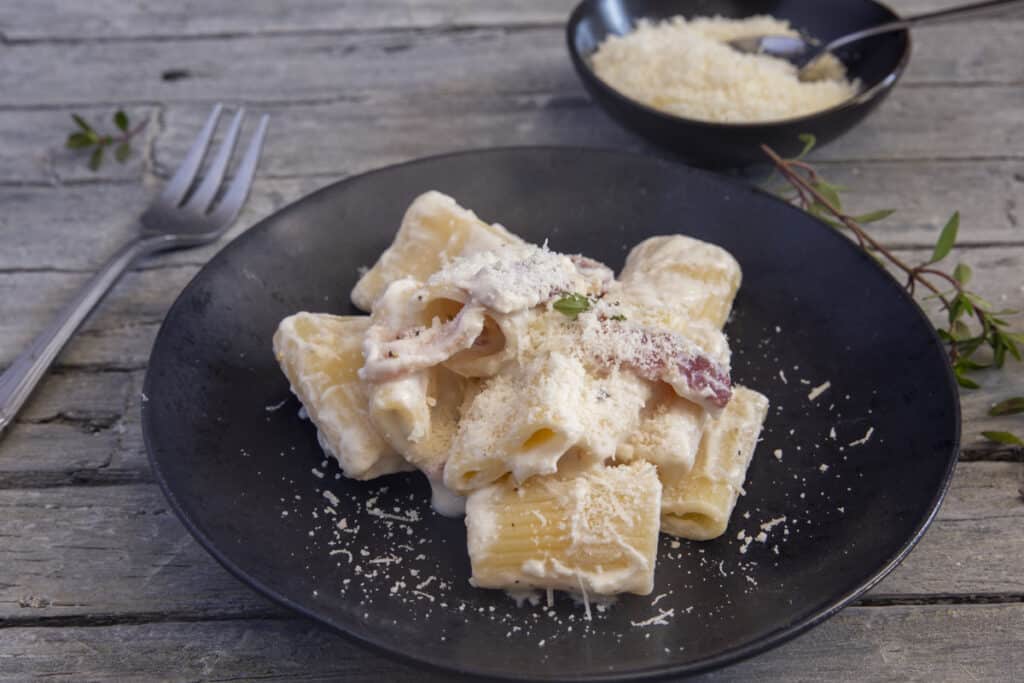 Pancetta pasta with parmesan on a black plate.
