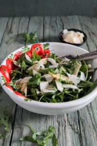 Arugula salad in a white and red bowl.