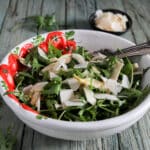 Arugula salad in a white and red bowl.