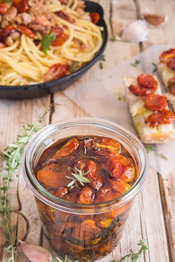 Pasta in a black pan and roasted tomatoes in a jar.