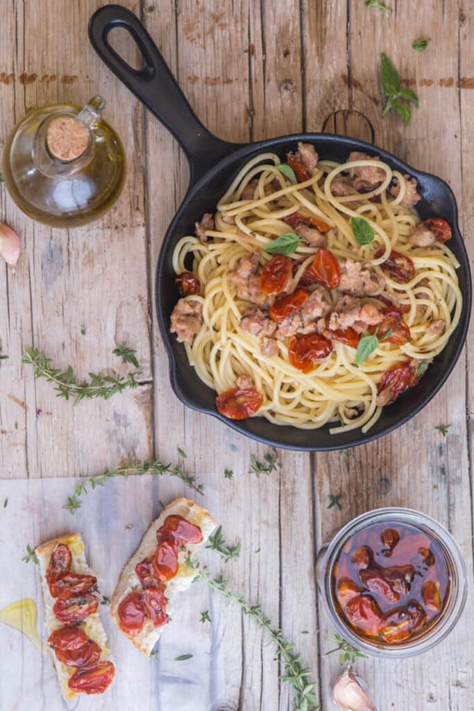 Pasta in a black pan and roasted tomatoes in a jar.
